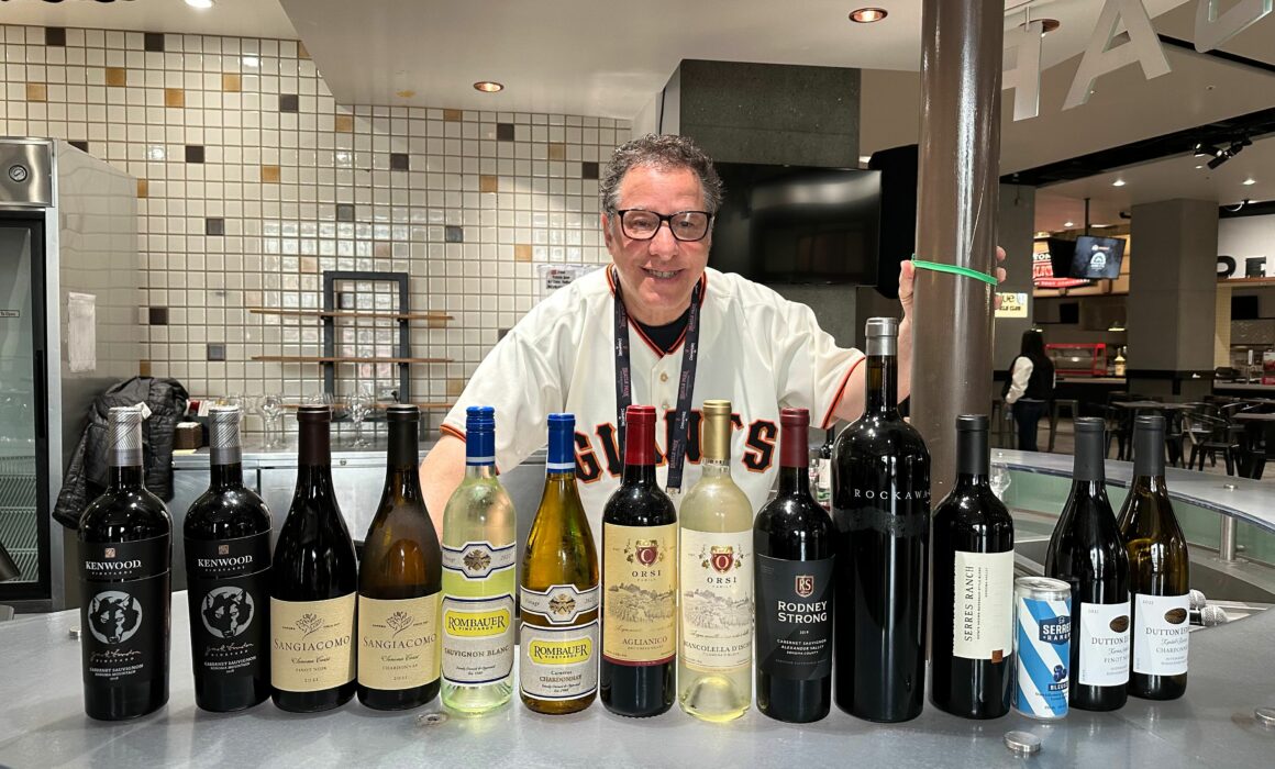 Man standing behind a bar, with 13 bottles of wine in front of him